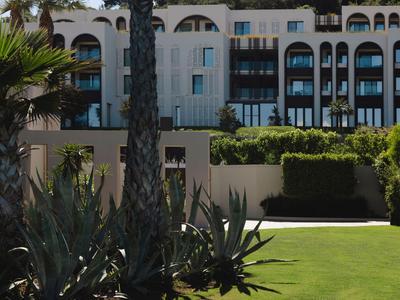Moderner Hotelkomplex mit weißer Fassade, grünen Pflanzen und gepflegtem Rasen im Vordergrund.