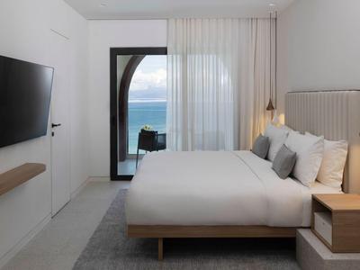 Modernes Hotelzimmer mit großem Bett, Meerblick und neutraler Dekoration.