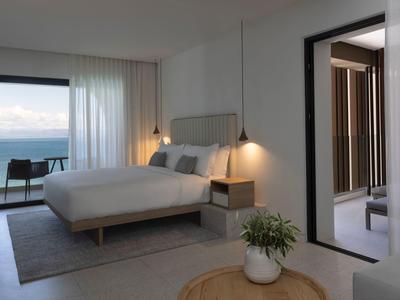Hell eingerichtetes Hotelzimmer mit Meerblick, Bett, Nachttischlampen und Balkon.
