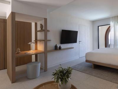 Modern eingerichtetes Hotelzimmer mit Doppelbett, Wand-TV und Arbeitsbereich mit Holzregalen.