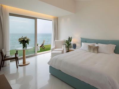 Helles Hotelzimmer mit großem Bett und Meerblick durch eine Glastür.