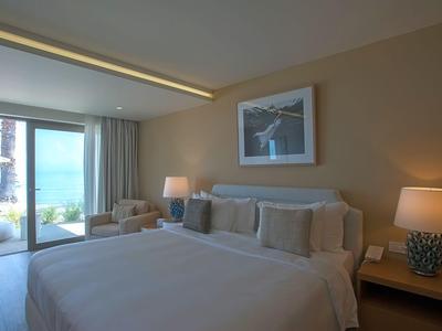 Helles Hotelzimmer mit großem Bett, Nachtlampen und Blick auf Terrasse und Meer.