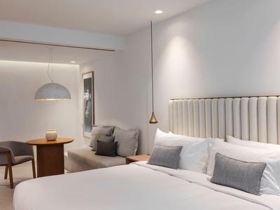 Modernes Hotelzimmer mit großem Bett, Nachttischen, Stühlen und Deko in neutralen Farben.