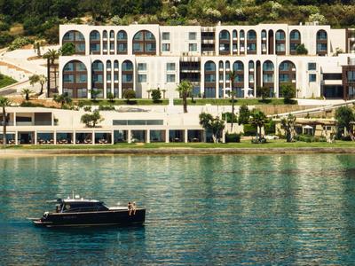 Modernes Hotel am Wasser mit großen Fenstern und Bootsfahrzeug auf ruhigem Meer.