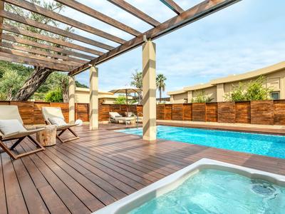 Hotelterrasse mit Holzdeck, Whirlpool, Pool und Sitzbereich unter einem Glasvordach.