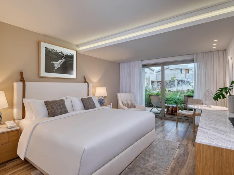 Modernes Schlafzimmer mit großem Bett, hellen Holzmöbeln und Glasfenstern zum Garten.