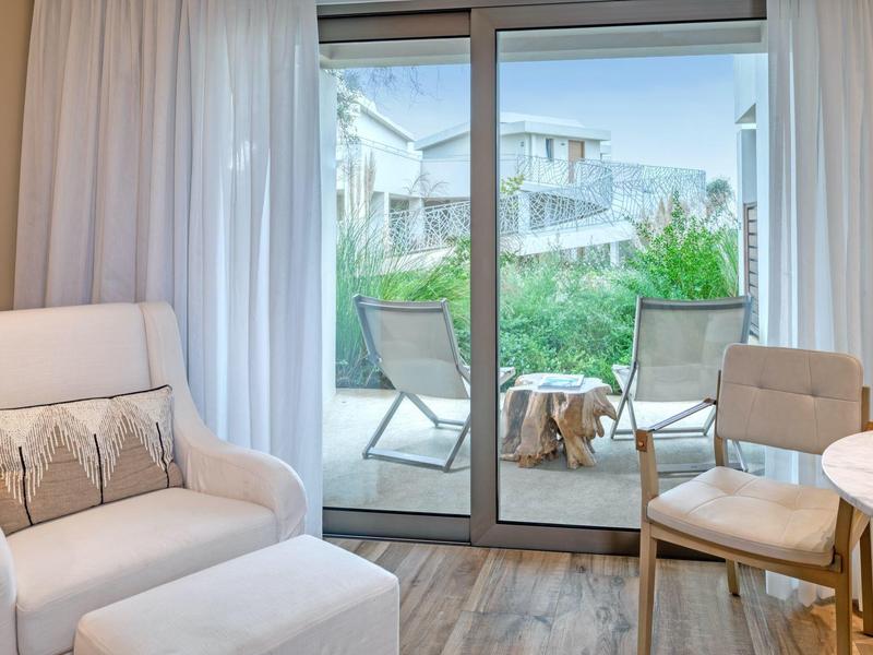 Helles Wohnzimmer mit weißen Möbeln und Blick auf Terrasse mit Garten und zwei Stühlen.