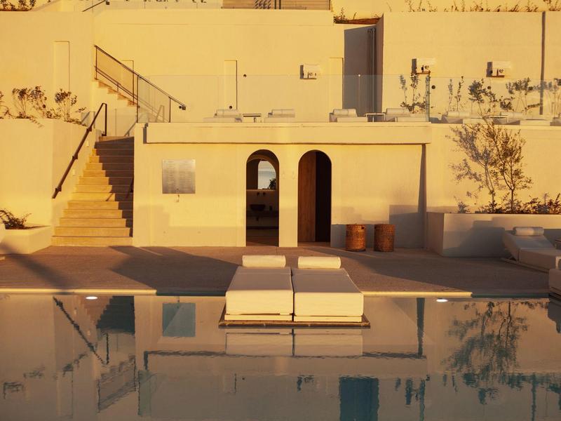 Modernes Gebäude mit Stufen, zwei Bögen und Sonnenliegen vor einem ruhigen Pool bei warmem Licht.