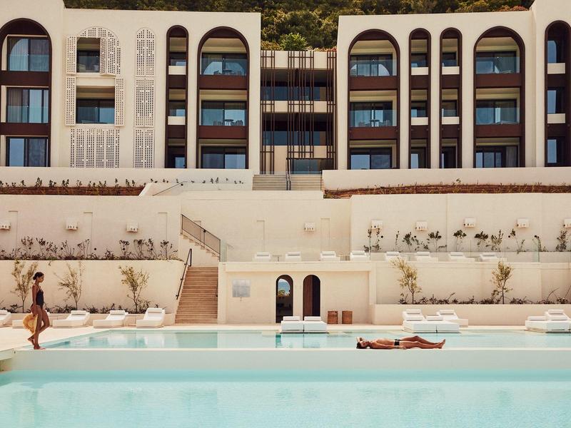 Moderner Pool vor weißem Gebäude mit großen, rundbogigen Fenstern und Pflanzen an der Wand.