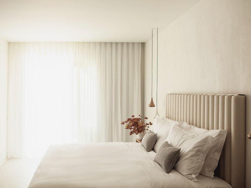 Helles Schlafzimmer mit großem Bett, hellen Vorhängen und minimalistischer Dekoration.