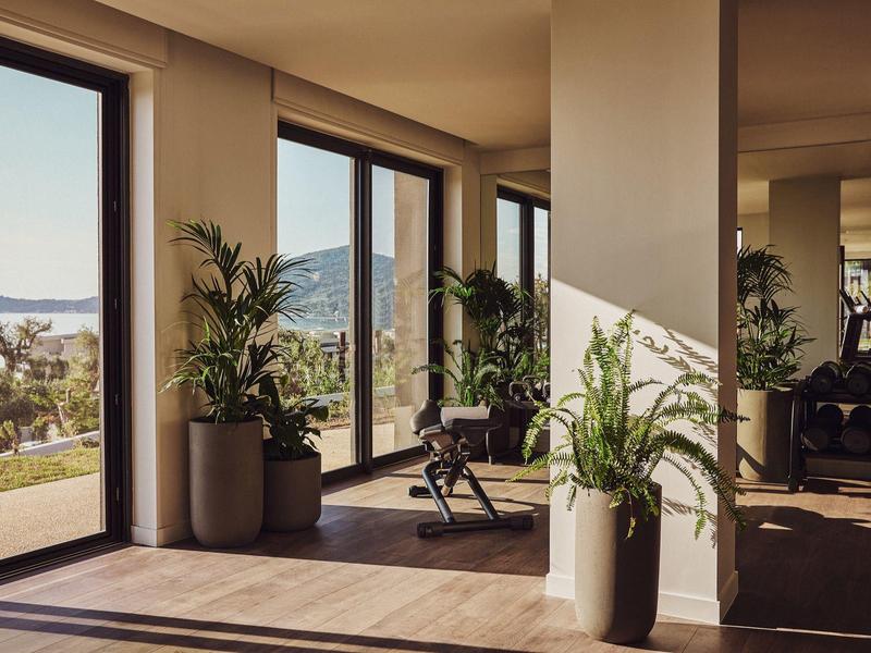 Helles Wohnzimmer mit großen Fenstern, Holzfußboden, grünen Pflanzen und Blick auf Berge und See.