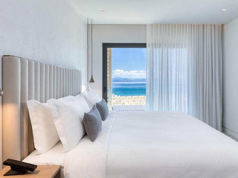 Helles Schlafzimmer mit großem Bett, weißen Wänden und Meerblick durch Schiebetür.