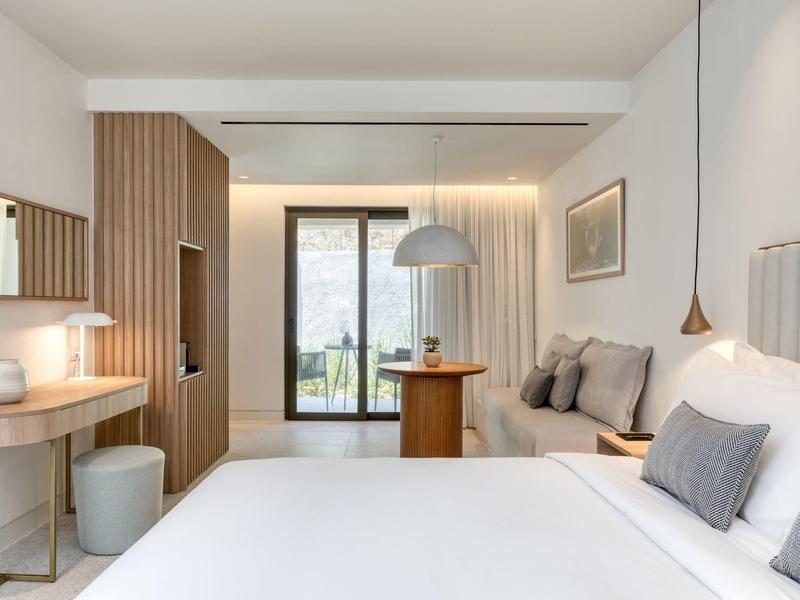 Helles Schlafzimmer mit weißer Bettdecke, Holzschrank, Balkon und modernem Lampendesign.