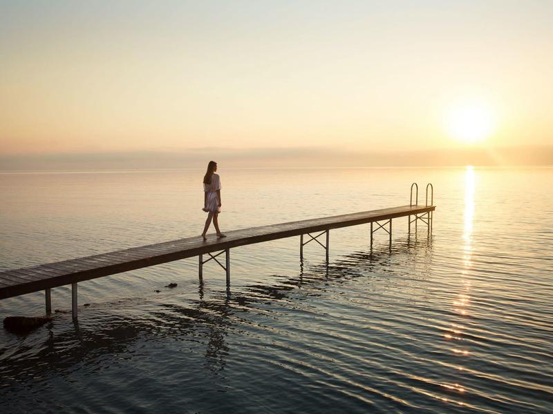 Eine Person geht auf einem langen Steg über ruhiges Wasser bei Sonnenuntergang.