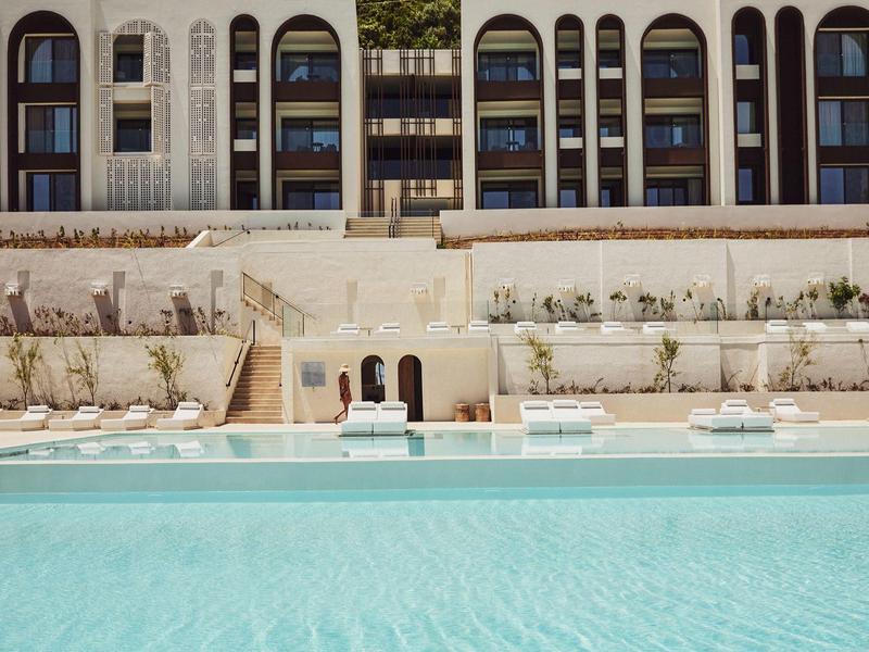 Großer Außenpool vor mehrstöckigem Hotel mit Balkonen und Liegestühlen am Rand.