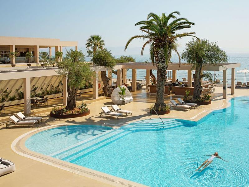 Hotelpool mit Palmen, Liegestühlen und Meerblick bei sonnigem Wetter am späten Nachmittag.