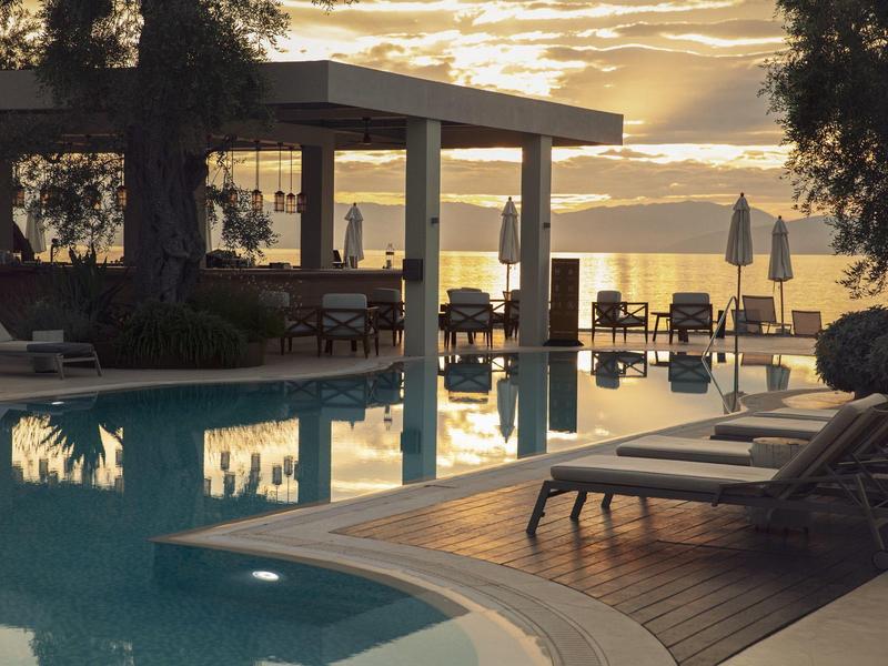 Ein ruhiger Poolbereich mit Liegestühlen und Pergola, Sonnenuntergang spiegelt sich im Wasser.