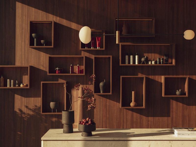 Holzwand mit rechteckigen Regalen, Vasen und Dekor, davor weißer Tisch mit Blumenarrangement.