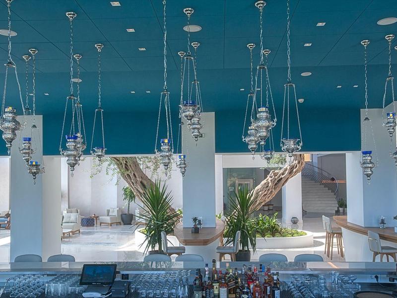 Großer Innenraum mit blauem Himmel-Decke, weißen Säulen, Hängeleuchten und Pflanzen in heller Atmosphäre.