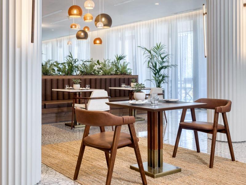 Modernes Esszimmer mit großen Fenstern, Holzstühlen, Teppich und hängenden Kupferlampen.