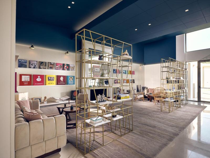 Moderner Verkaufsraum mit blauer Decke, goldfarbenen Regalen und beigen Sitzmöbeln auf grauem Teppich.