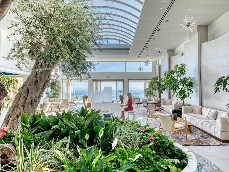 Helle Lounge mit großen Fenstern, Pflanzenarrangements und moderner, bequemer Einrichtung.