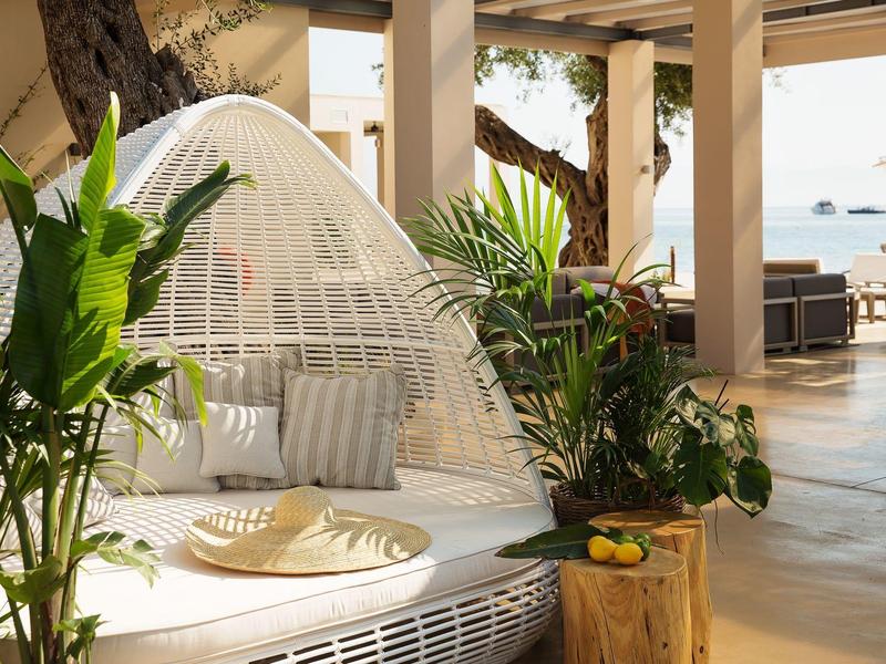 Gemütlicher weißer Daybed mit Moskitonetz auf offener Terrasse, umgeben von grünen Pflanzen.