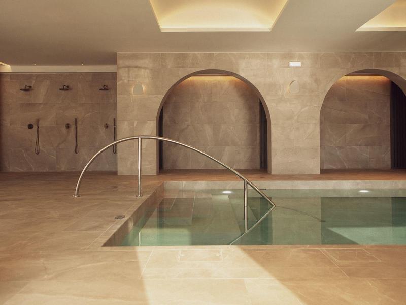 Moderner Innenpool mit geschwungenem Edelstahlgeländer und sanfter Beleuchtung in warmen Tönen.