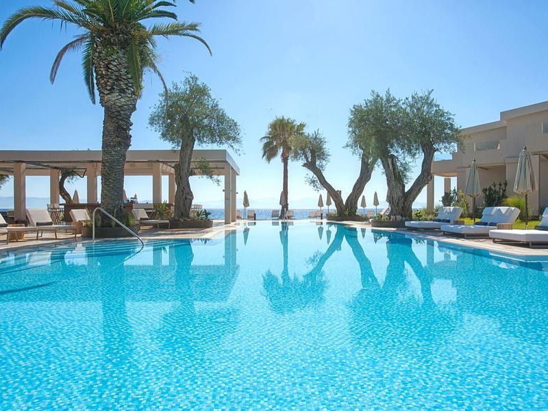 Großer blauer Pool mit Palmen und Lounge-Bereich unter klarem Himmel am Meer.