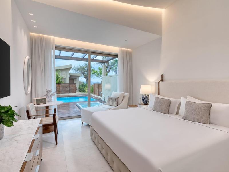 Helles Schlafzimmer mit großem Bett, weißen Wänden, Holzakzenten und Blick auf einen Pool außen.