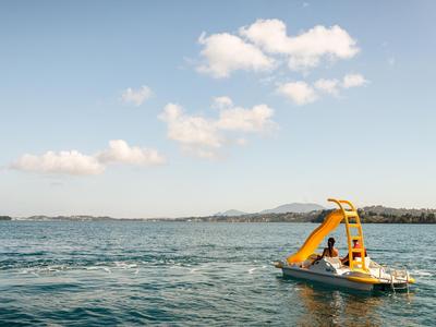 Pedalò con scivolo giallo su lago calmo sotto cielo blu con nuvole