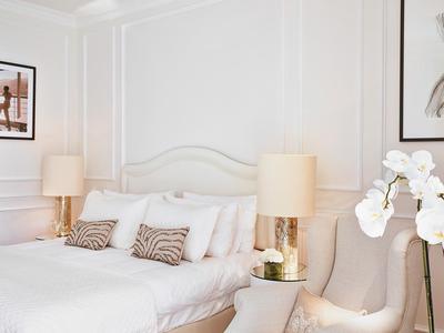 Elegantes Schlafzimmer mit großem weißen Bett, zwei Nachttischen, Lampen und Orchidee im Vordergrund.