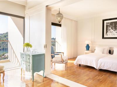 Helles Schlafzimmer mit Doppelbett, Holzfußboden, weißer Gardine und blauer Kommode mit Vase.