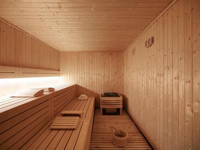 Innenraum einer Sauna mit Holzwänden, Holzliegen, kleiner Holzkiste und Saunakübel auf Holzfußboden.