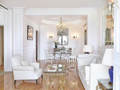 Helles Wohnzimmer mit weißen Möbeln, goldfarbenem Tisch, Kronleuchter und großem Spiegel.