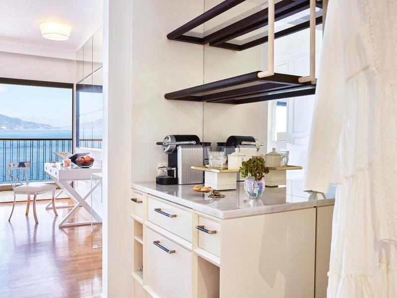 Moderne Küche mit weißer Arbeitsplatte, Kaffeemaschine und Blick auf Balkon mit Meer und Tisch.