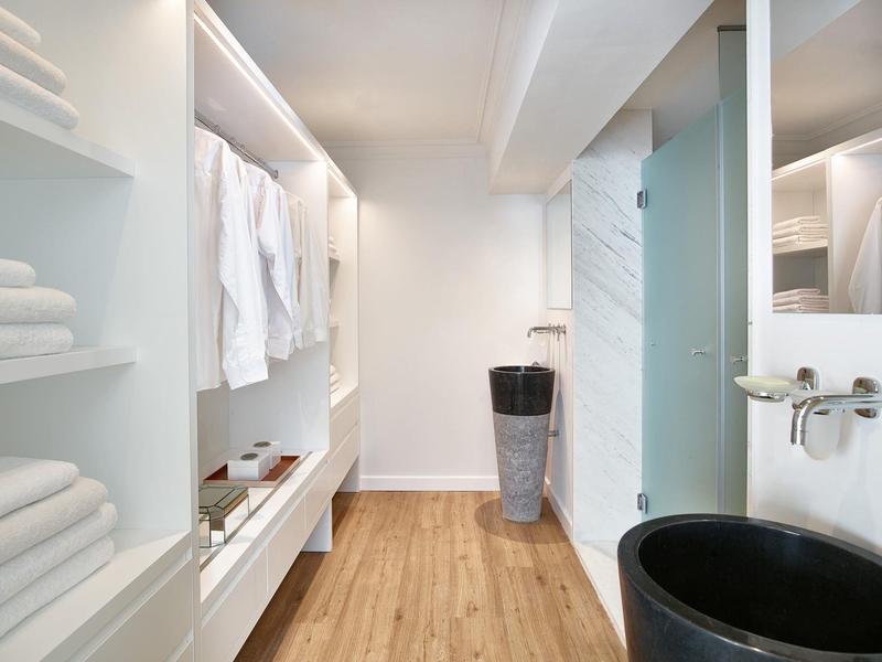 Moderner, heller Badezimmerbereich mit Holzboden, offener Garderobe und Glasdusche.