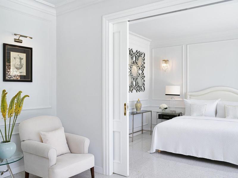 Helles Schlafzimmer mit weißem Bett, bequemen Sessel, Zierpflanze und modernem Wanddekor.