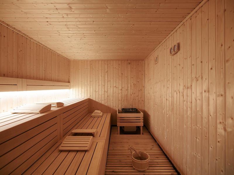 Innenraum einer Sauna mit Holzwänden, Holzliegen, kleiner Holzkiste und Saunakübel auf Holzfußboden.