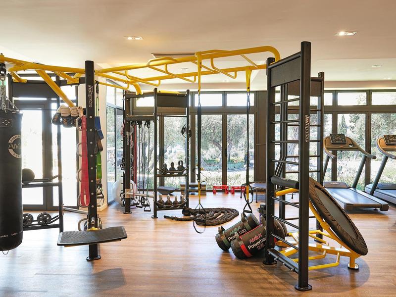 Moderner Fitnessraum mit Holzboden, großen Fenstern und vielfältigen Trainingsgeräten in Gelb und Schwarz.