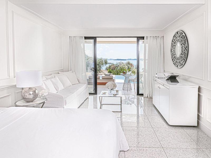 Helles, modernes Wohnzimmer mit weißem Sofa, Glas-Couchtisch und Blick auf Terrasse und Meer.