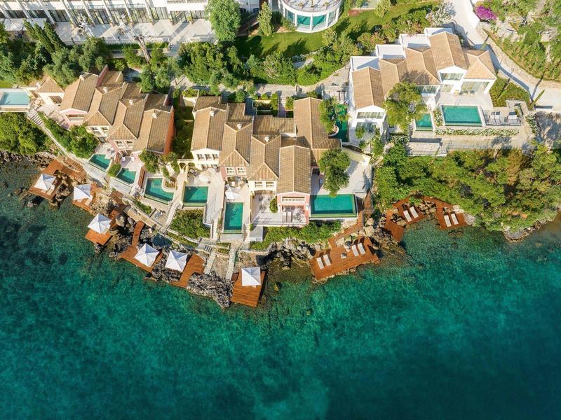 Luxuriöse Strandvillen mit Pools und Stegen am türkisblauen Meer in tropischer Anlage.