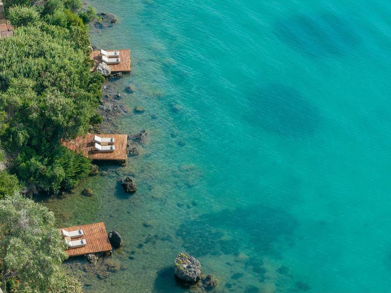 Mehrere Holzliegen auf Plattformen am türkisfarbenen Wasser neben einem bewaldeten Ufer.