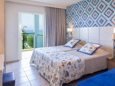Hell eingerichtetes Hotelzimmer mit Doppelbett und Blick auf eine Terrasse.