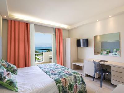 Helles Hotelzimmer mit Doppelbett, Schreibtisch, Fernseher und Blick auf das Meer.