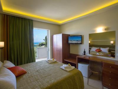 Hell eingerichtetes Hotelzimmer mit großem Bett, Schreibtisch und Fenster mit Meeresblick.