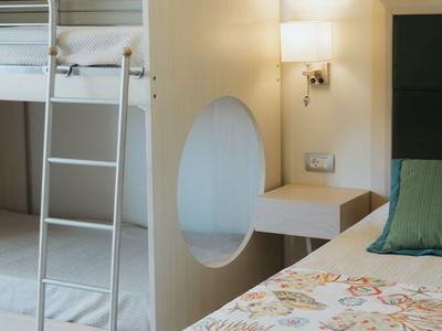 Hotelzimmer mit Etagenbett, dekorativem Einzelbett und beleuchtetem Nachttisch.