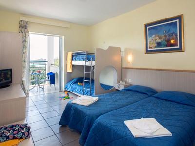 Helles Hotelzimmer mit Doppelbett, Etagenbett, Fliesenboden und Balkon mit Meerblick.