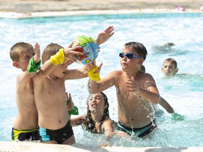 Kinder spielen fröhlich mit Wasser in einem Hotelpool an einem sonnigen Tag.