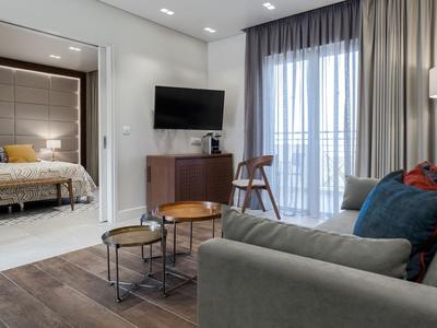Modern eingerichtetes Hotelzimmer mit Schlafzimmer, Sofa und Balkon mit Vorhängen.